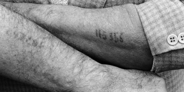 A Holocaust survivor displays the numerical tattoo stamped on his arm, a physical remnant of his imprisonment in a World War II Nazi concentration camp, during ceremonies commemorating the 50